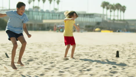Happy-kid-scoring-goal-while-playing-soccer-with-friend-on-beach